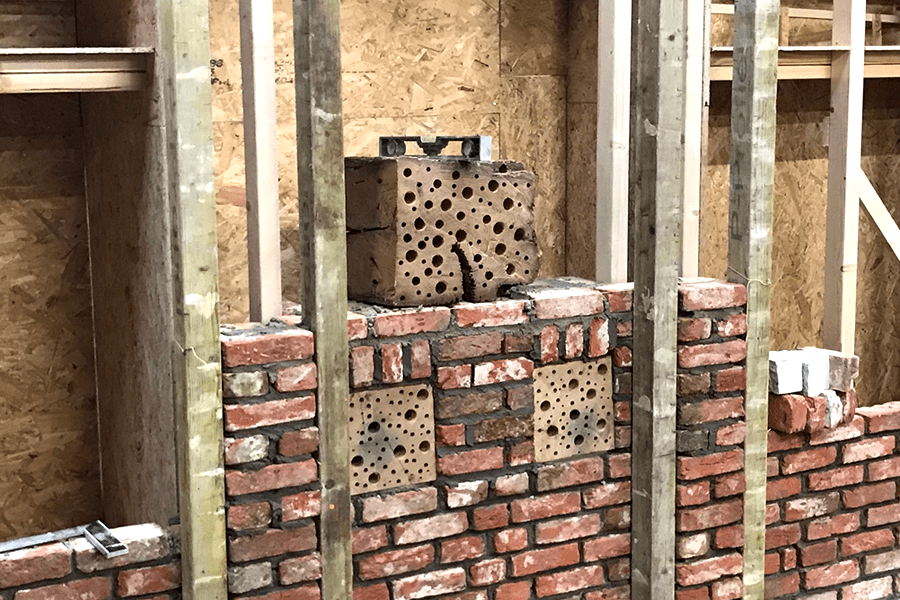 A brick wall under construction with integrated bee bricks, surrounded by wooden framing.