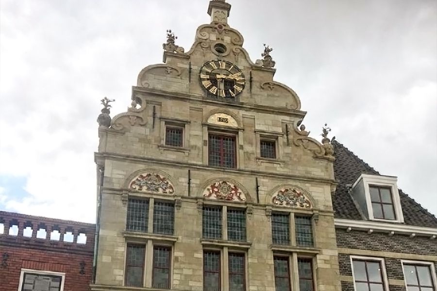 A historic stone building with an elaborate gabled facade, a large clock face, and decorative carvings.