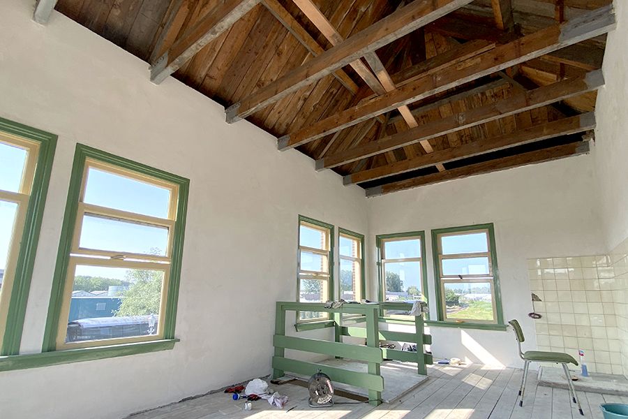 Unfinished room with white walls, green window frames, and exposed wooden ceiling beams.