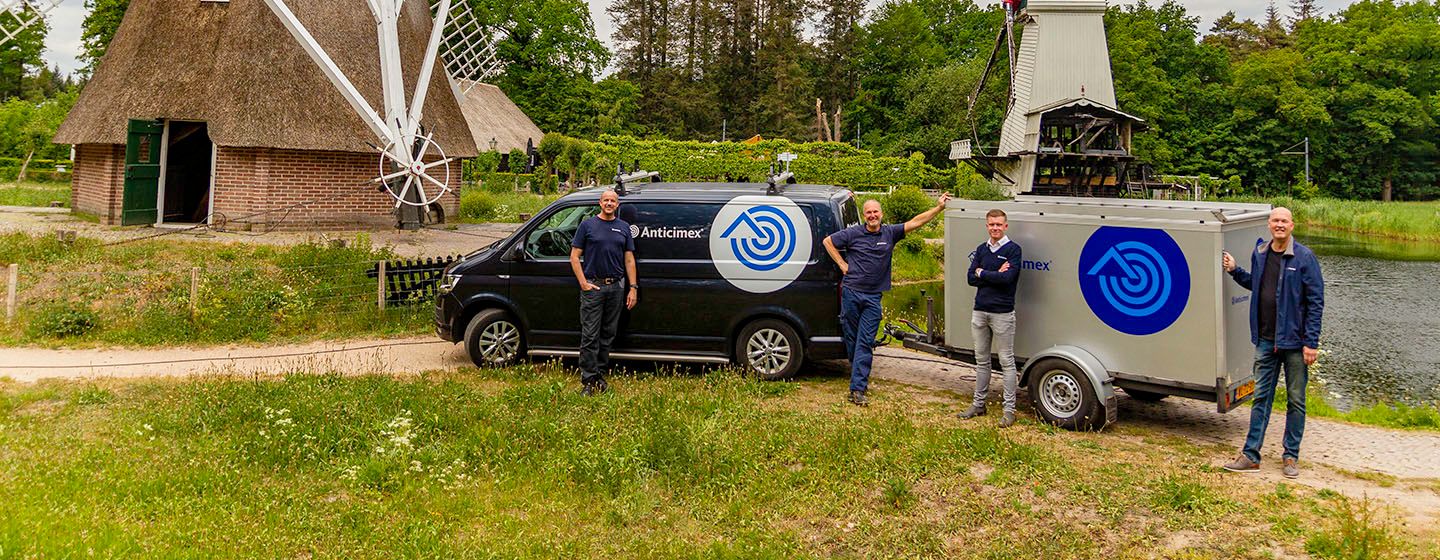 Three smiling men stand next to a black van and a grey trailer, both branded with a blue Borexmex logo, outdoors by a pond.