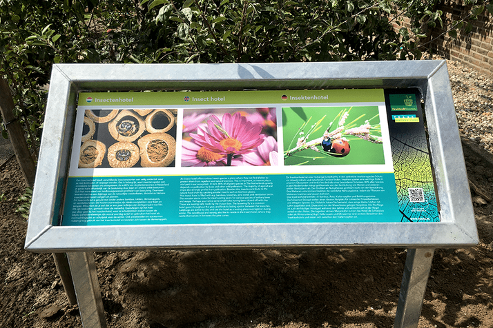An outdoor information sign about insect hotels, featuring three photos: an insect habitat, a pink flower, and a ladybug.