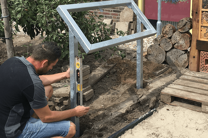 Man leveling a metal frame post in the ground, next to an insect hotel.