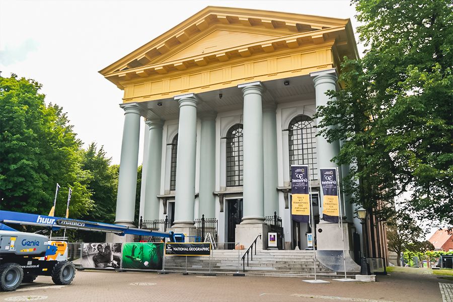 A classical-style building with a yellow pediment and columns, featuring National Geographic banners and a blue construction lift.