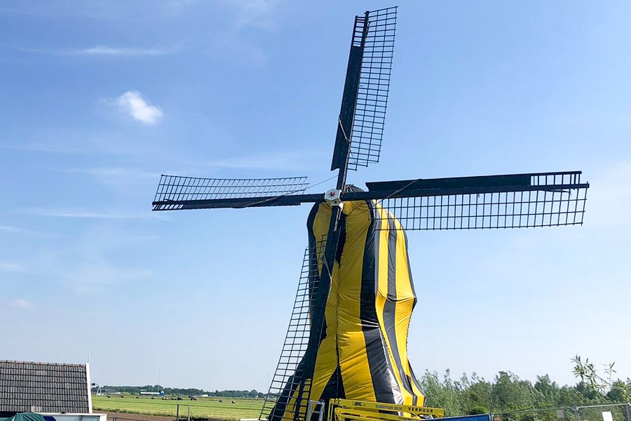 A windmill with a yellow and black striped body and black blades against a blue sky and green field.