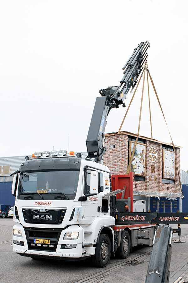 A Gabrielse truck's crane lifts a large, ornate brick insect hotel.