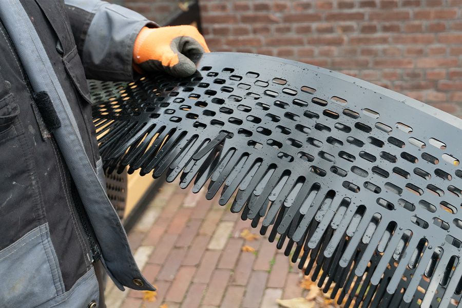 A person in an orange glove holds a black, perforated plastic strip with comb-like teeth.