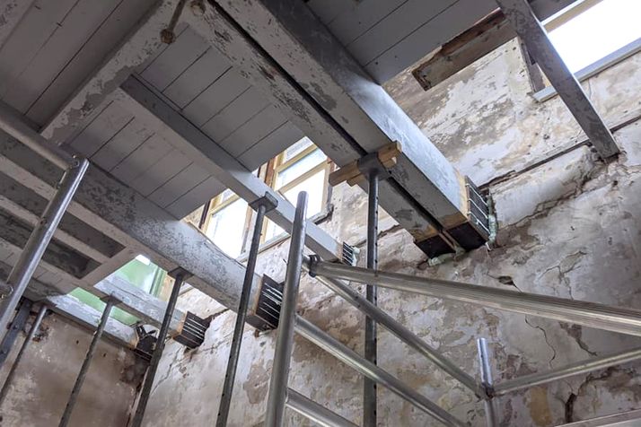 Scaffolding supports large wooden beams in a room under renovation.