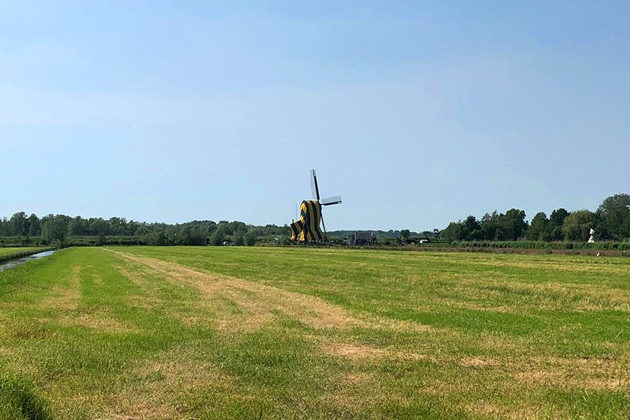 A green field with a yellow and black striped windmill under a clear blue sky.