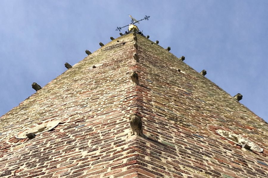 Low-angle view of a weathered brick church spire with many gargoyles under a blue sky.