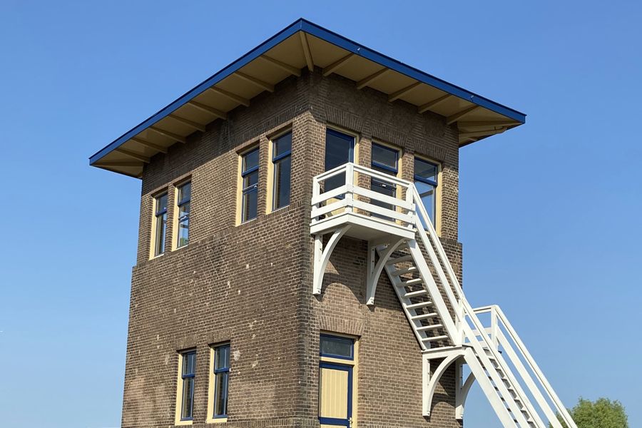 A dark brick tower with blue and yellow eaves and a white exterior staircase.