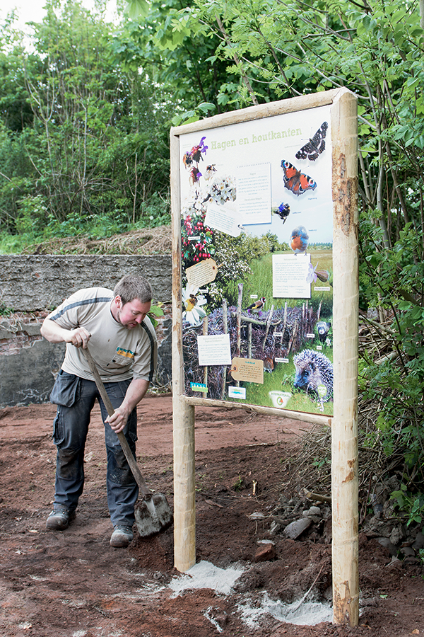 A man shovels dirt around a newly installed outdoor information sign about nature.