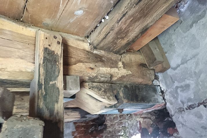 Weathered wooden beams and supports joined to a rough stone wall.