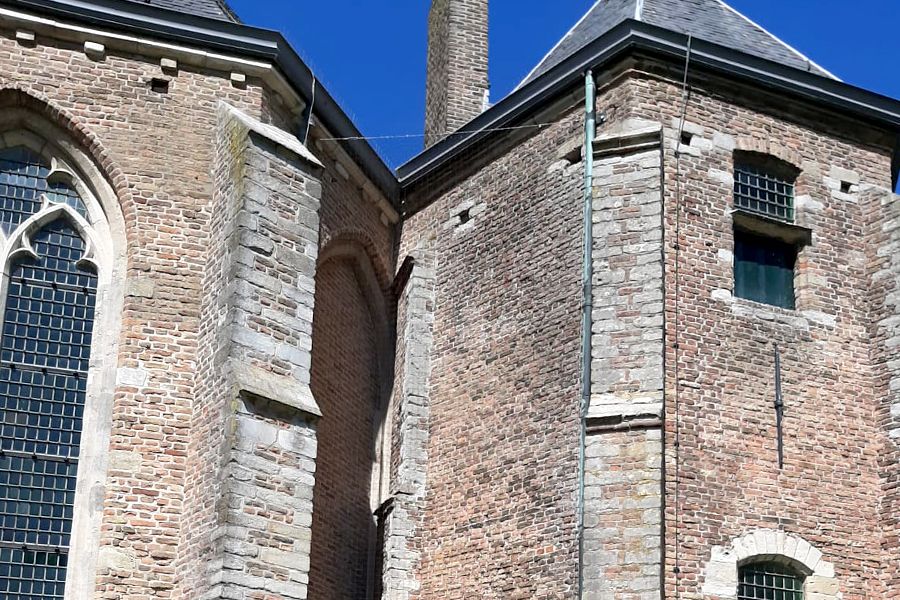 Detail of a historic brick building with a large Gothic window and smaller barred windows under a blue sky.