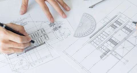 2 handen met pennen die aan het tekenen zijn op bouwtekeningen