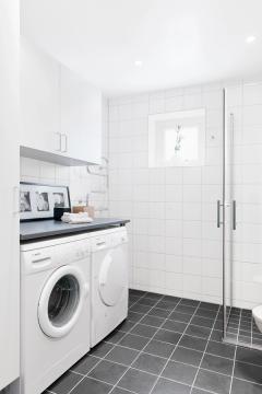 Vitt och grått kaklat badrum med dusch och tvättmaskin