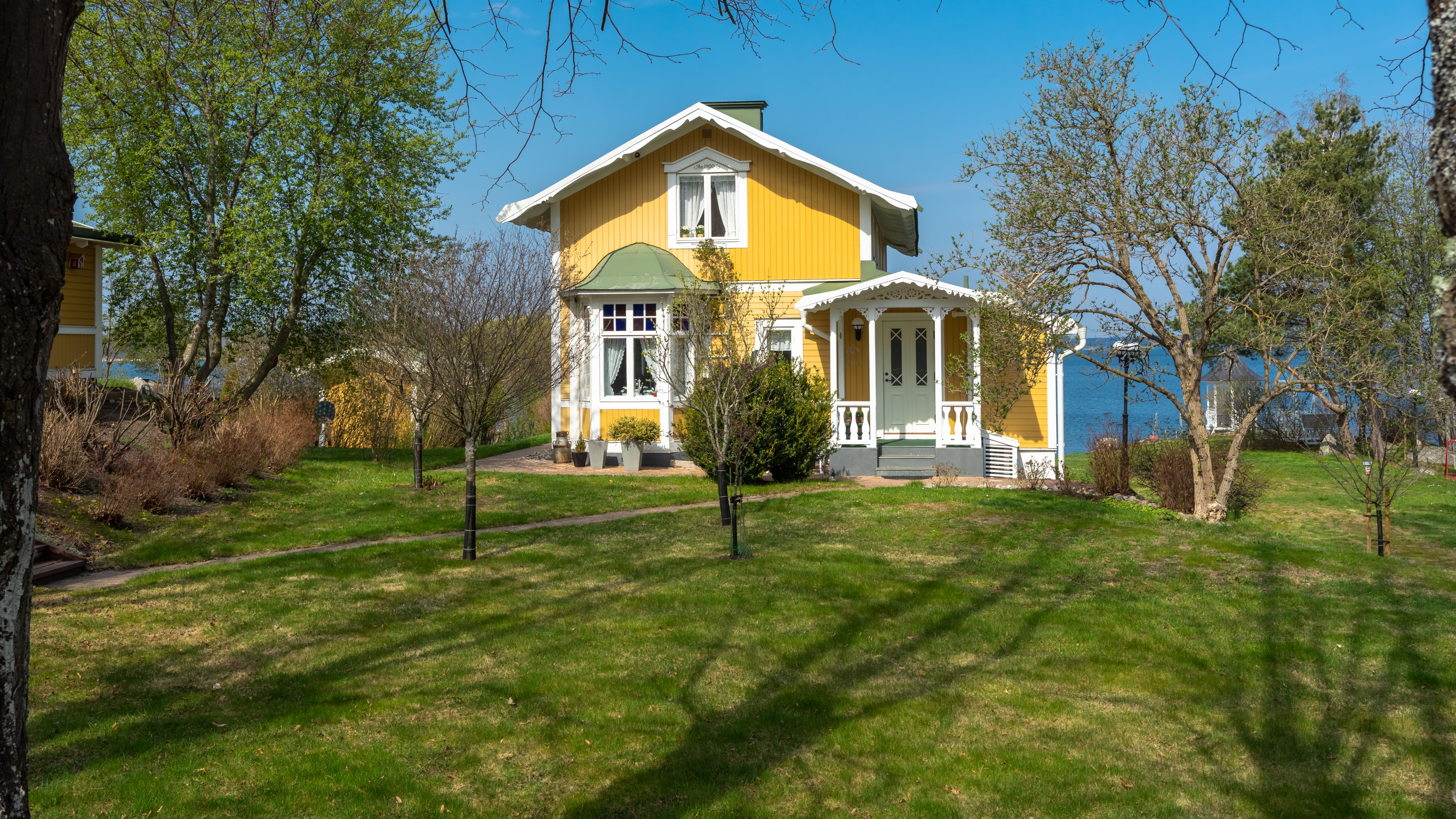 Gult trähus med vita knutar i en grön trädgård framför havet