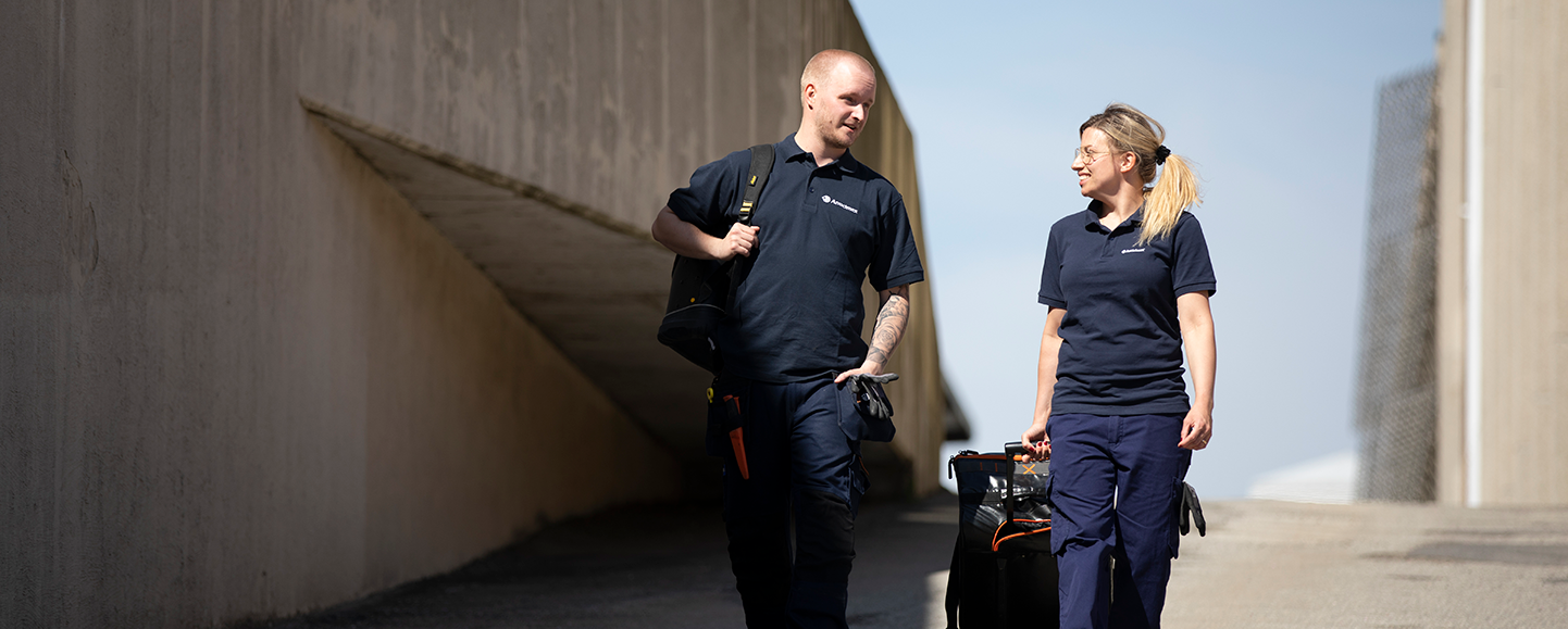 Två tekniker från Anticimex går mellan betongbyggnader med utrustning efter utförd fuktkontroll