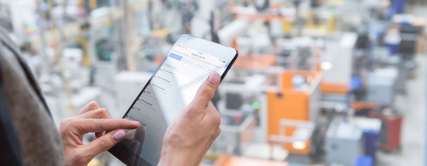 Kvinna håller i surfplatta i fabriksmiljö och utför digitalt egenkontrollsprogram