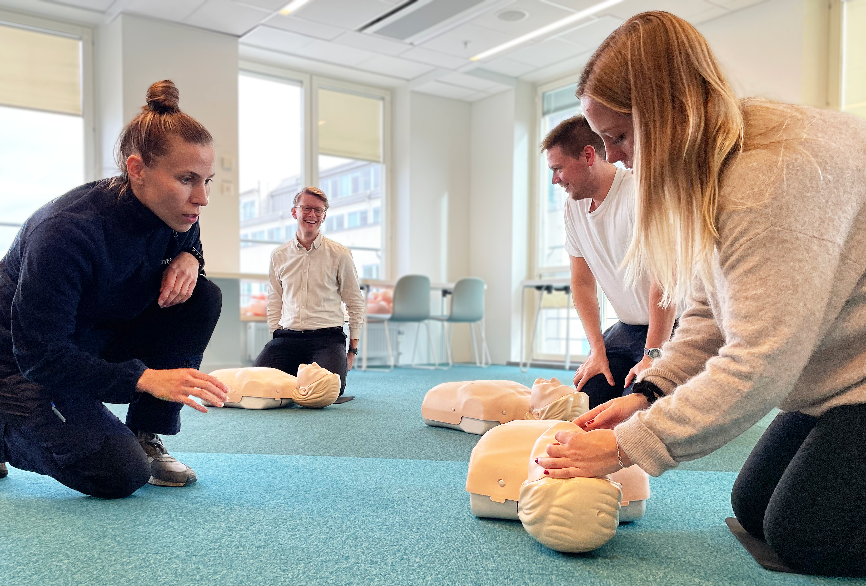 Anticimex-instruktör utbildar tre personer i hjärt- och lungräddning på dockor i ett rum med blått golv