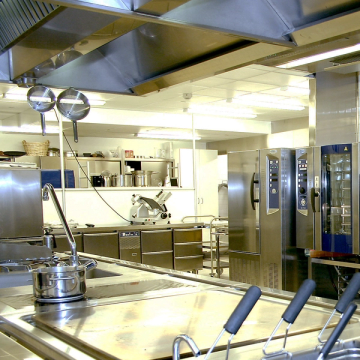 Modernt storkök med rostfria arbetsytor, kastruller, köksredskap och industriugnar.