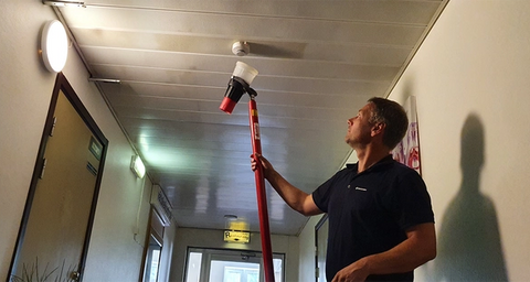 Anticimex brandskyddstekniker provar ett brandlarm i taket på en korridor