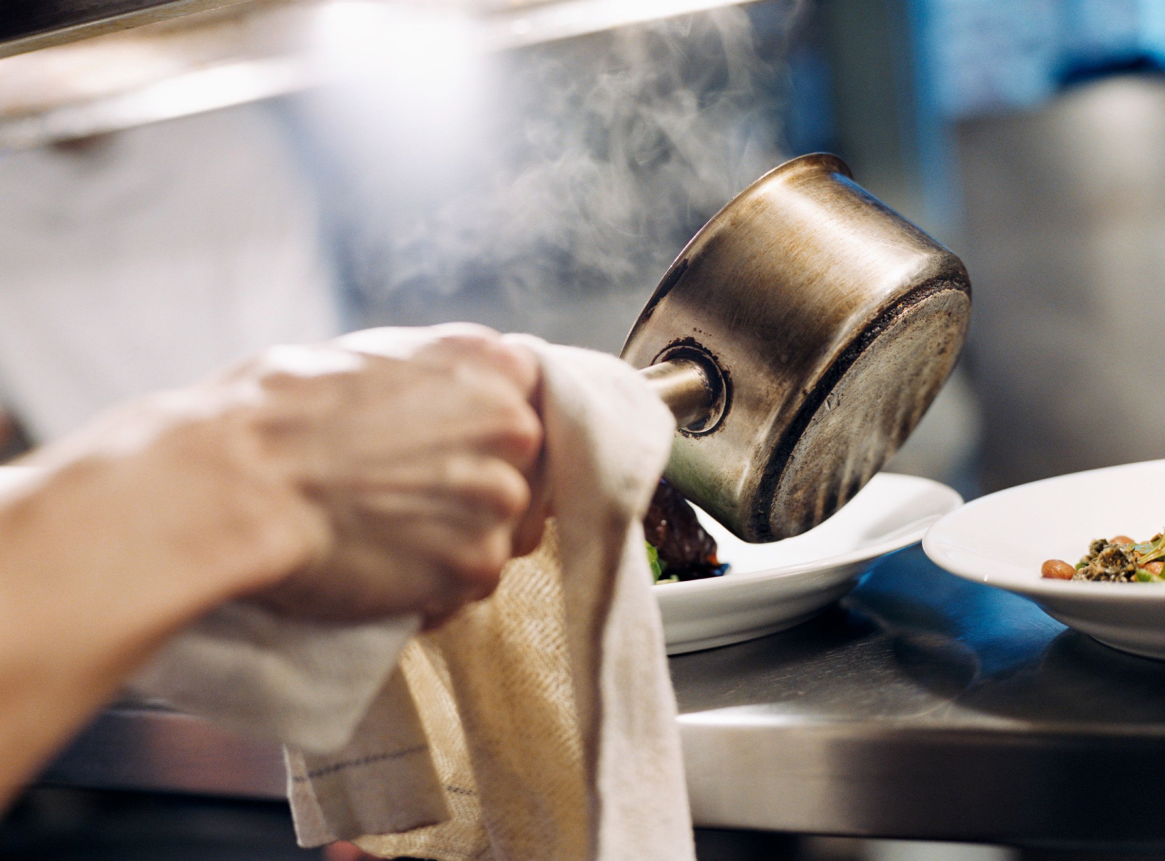 Hand som häller upp mat på en tallrik ur en kastrull i ett restaurangkök