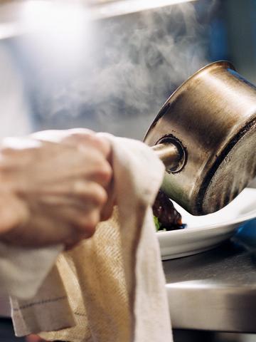 Hand som häller upp mat på en tallrik ur en kastrull i ett restaurangkök