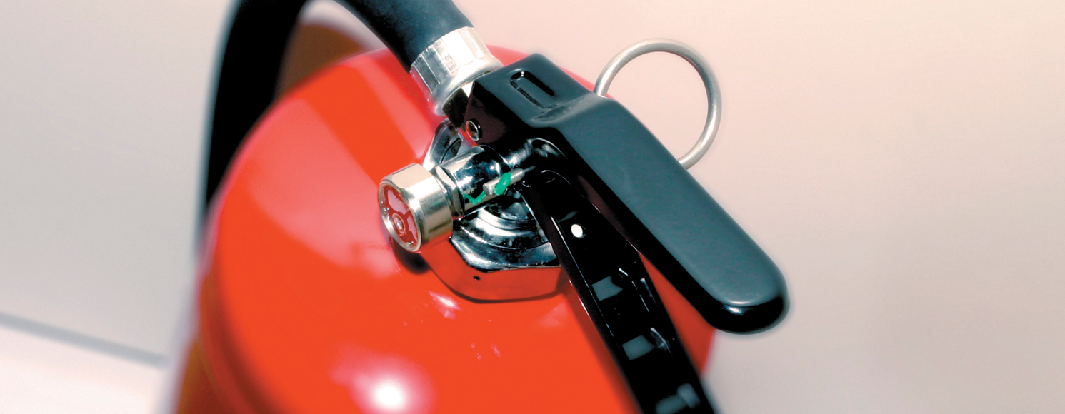 Närbild av toppen på en röd brandsläckare med svart handtag