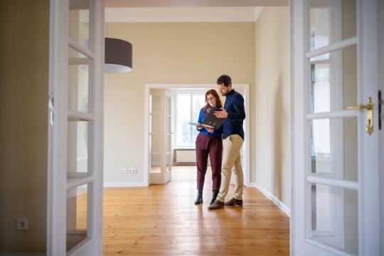 En man och en kvinna står i tomt rum i bostadsrätt och läser dokument