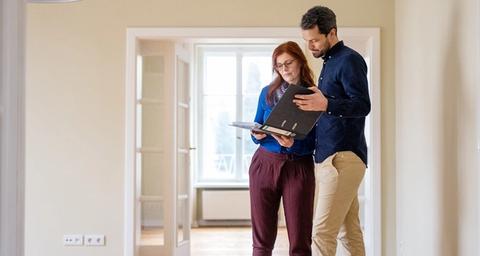 Par står mitt i ett rum i ljus lägenhet och inspekterar dokument för areamätning