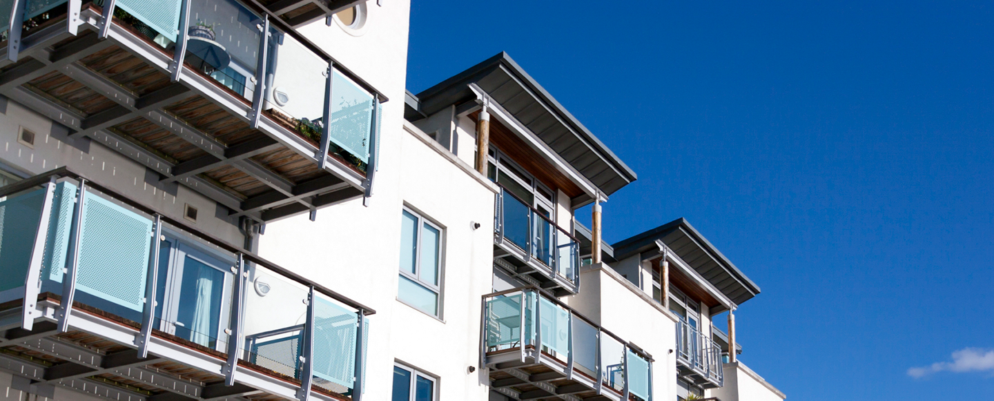 Vitt lägenhetshus med glasbalkonger med blå himmel i bakgrunden