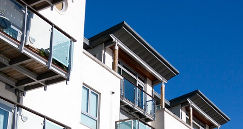 Vitt lägenhetshus med glasbalkonger med blå himmel i bakgrunden