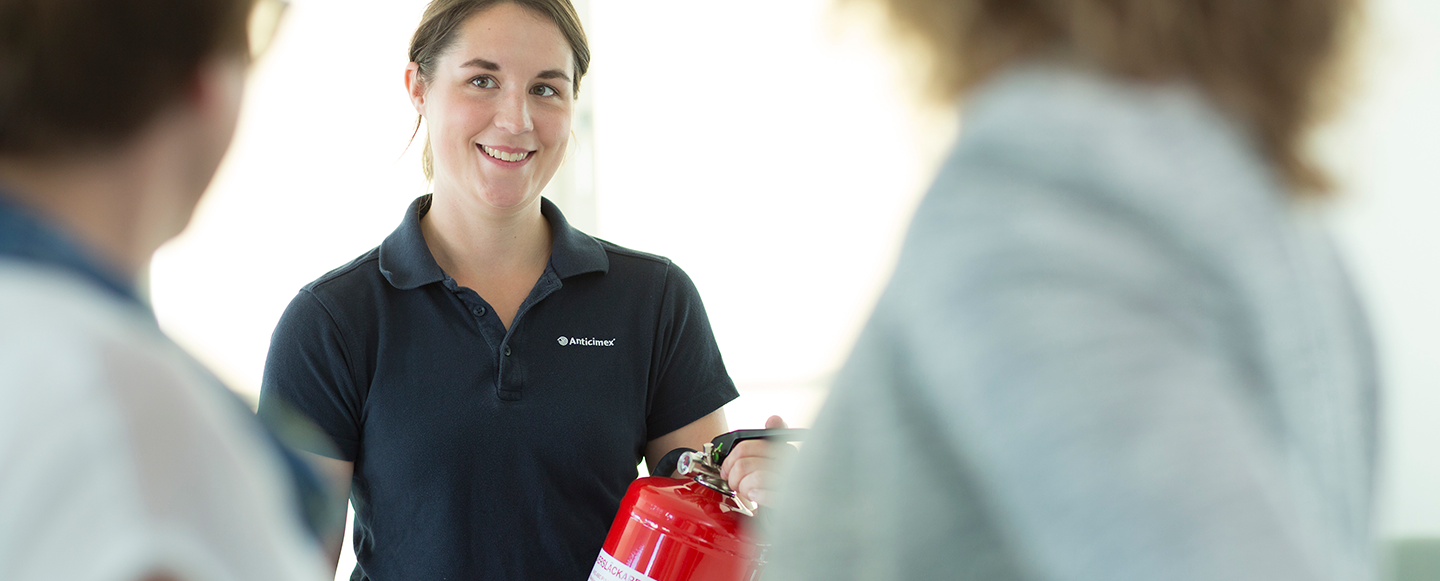 Anticimex tekniker håller i en brandsläckare och pratar om brandskydd med två personer i förgrunden