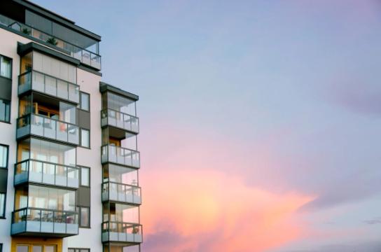 Exteriör på modernt lägenhetshus med glasbalkonger i solnedgång