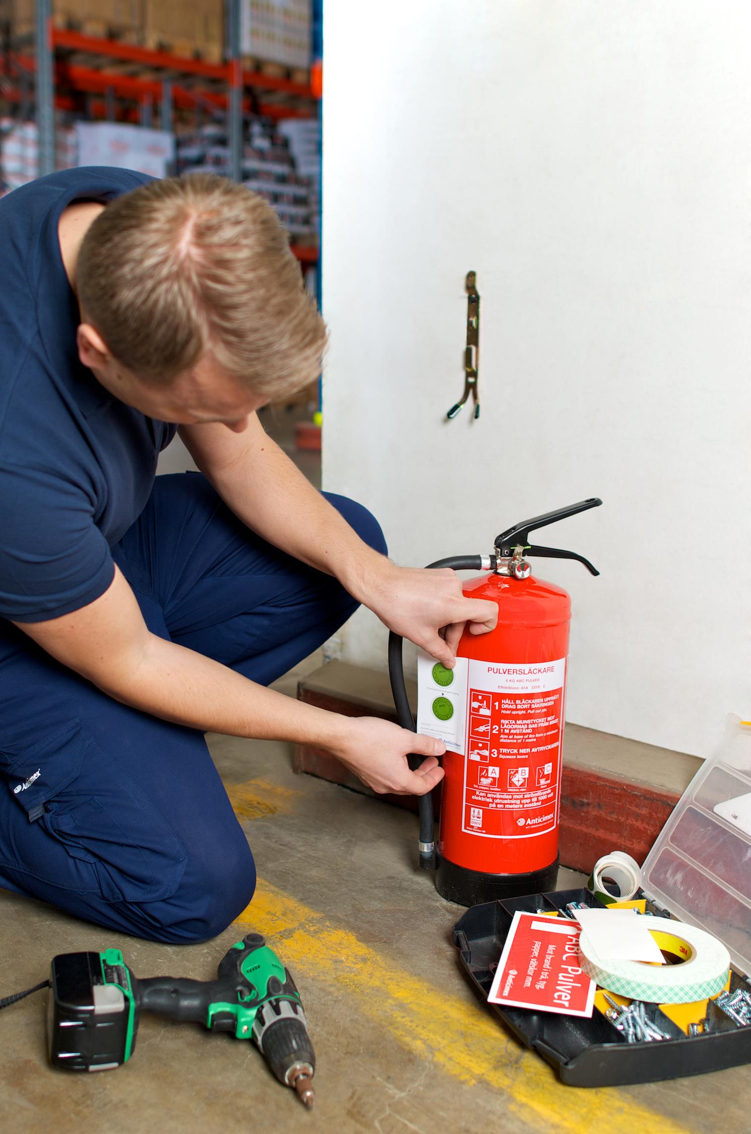 Anticimex tekniker utför service på en röd brandsläckare på ett golv