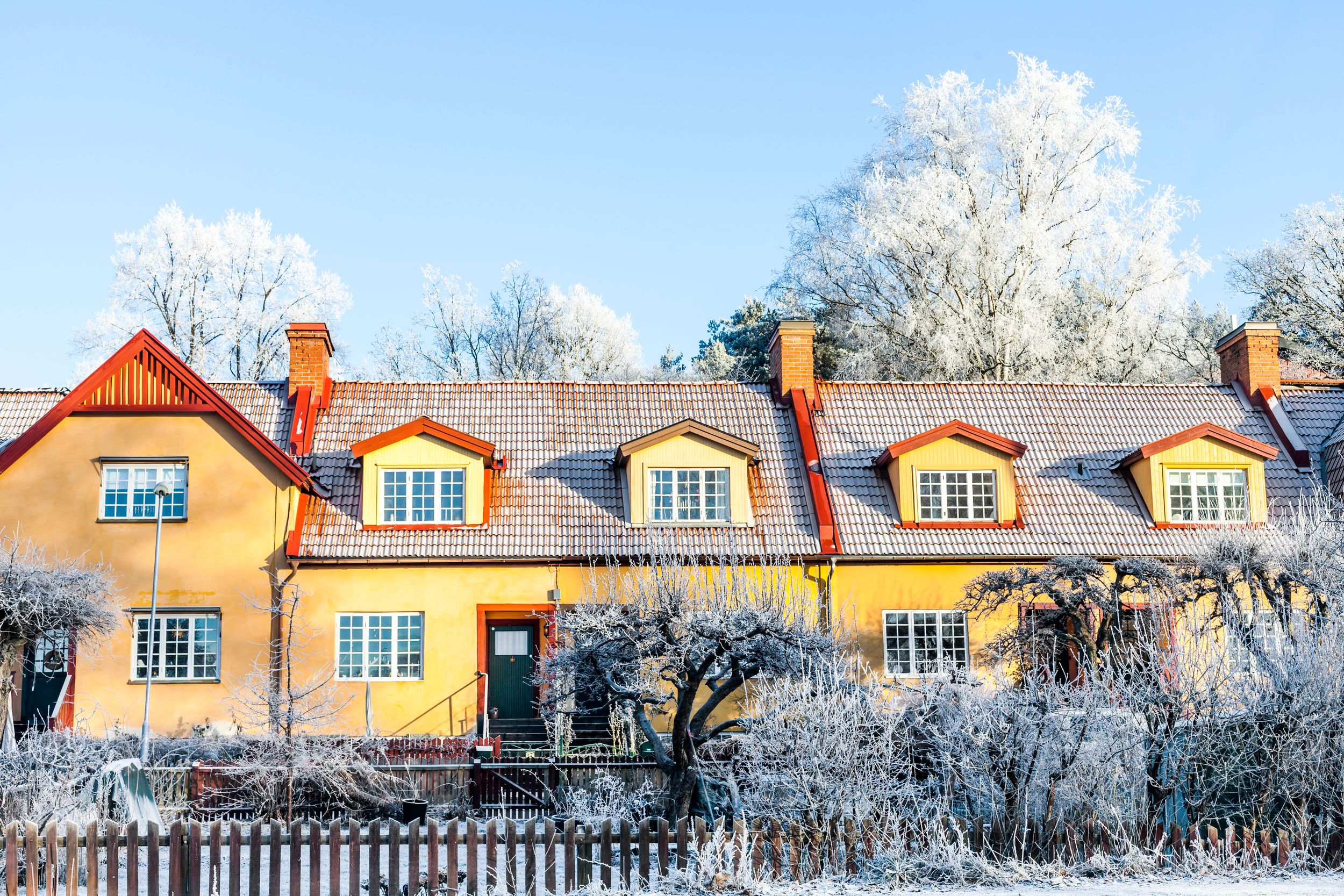 Gult hus med snö i trädgården och på taket - skydda huset mot frysskador