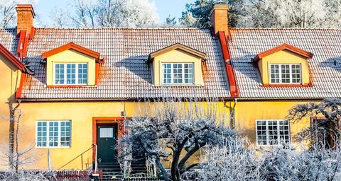 Gult hus med snö i trädgården och på taket - skydda huset mot frysskador