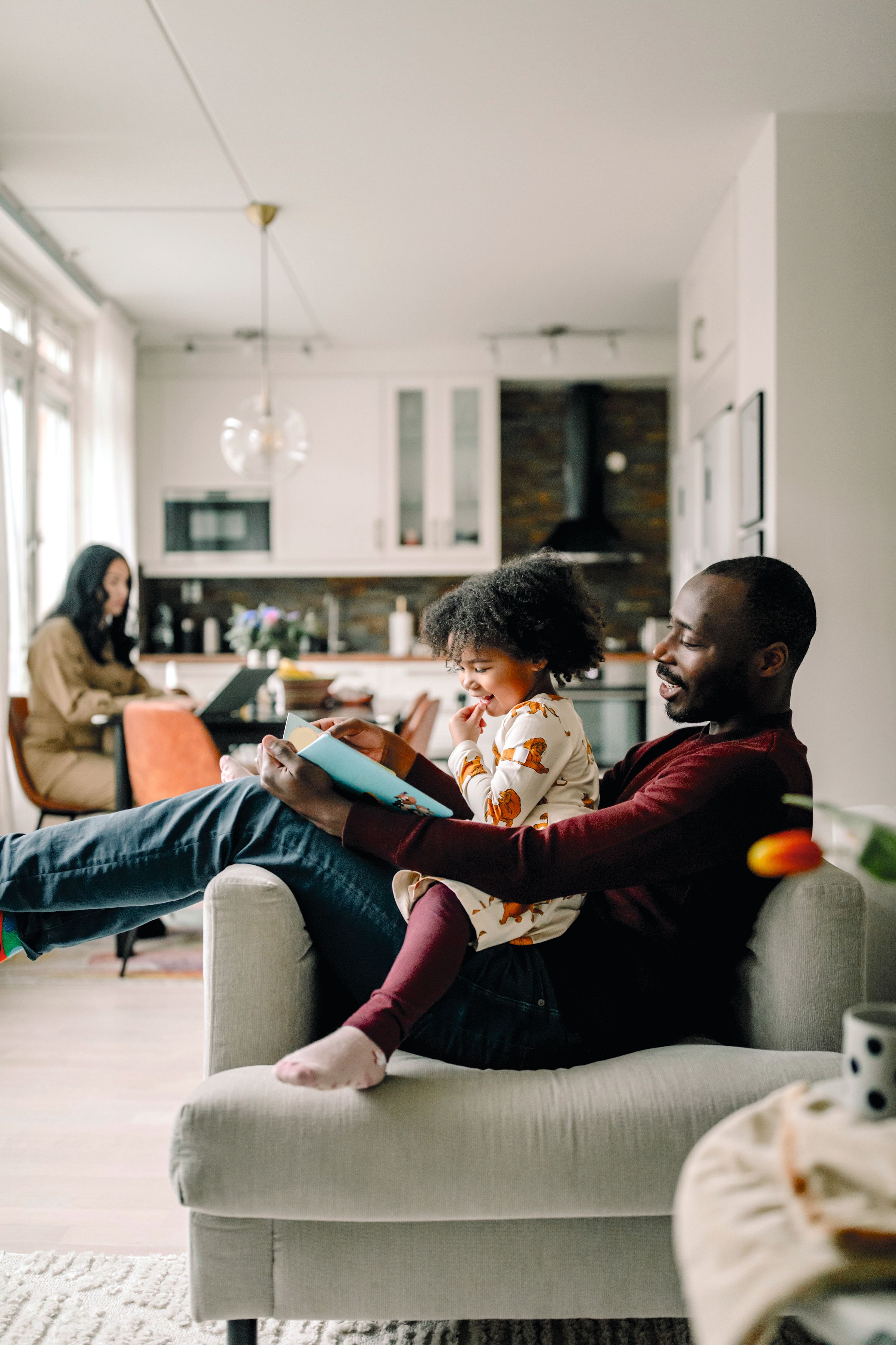 Familj i ett kök i villa med pappa som läser en bok för ett barn i fåtölj