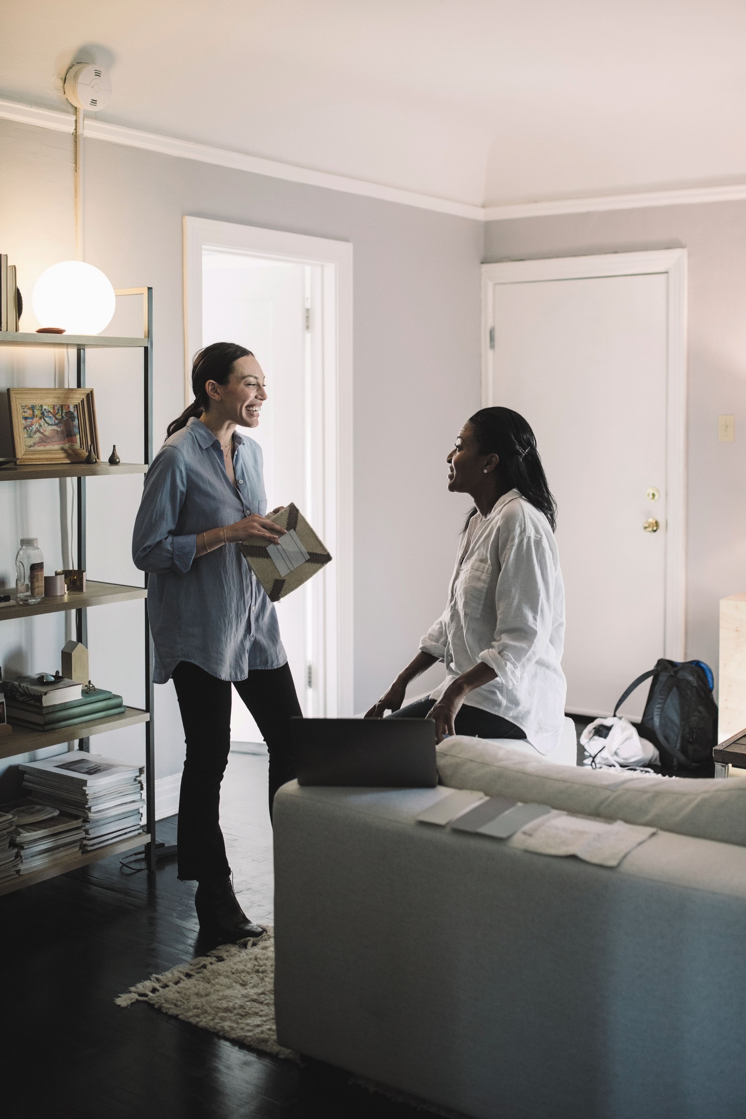 Två kvinnor samtalar om säljansvarsförsäkring i ett gråmålat vardagsrum i bostad