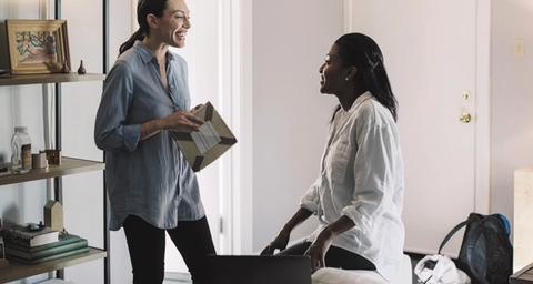 Två kvinnor samtalar om säljansvarsförsäkring i ett gråmålat vardagsrum i bostad