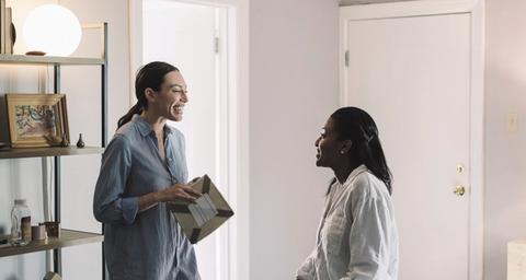 Två kvinnor samtalar i ett gråmålat vardagsrum i bostadsrätt