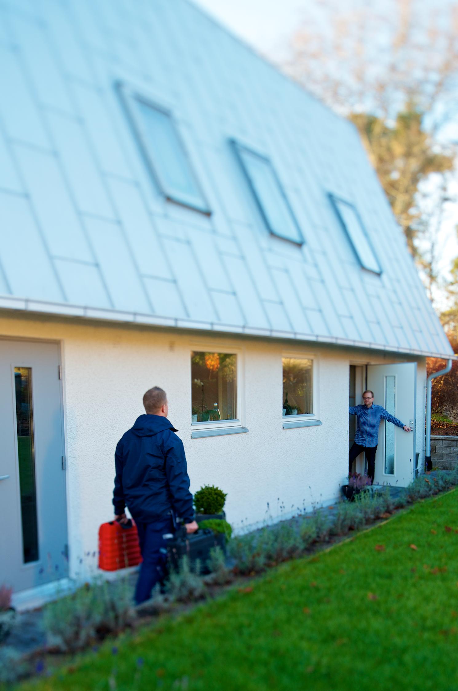 En tekniker från Anticimex på väg att göra överlåtelsebesiktning går mot dörr i vit stenvilla där en husägare står och väntar