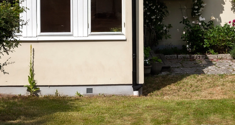 Svartvitt hus med rött tegeltak, träbalkong och blommande klätterväxt i en grönskande trädgård.