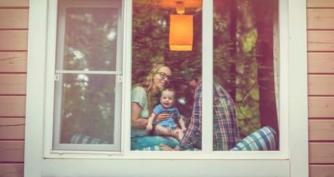 Familj med litet barn sitter i fönster i beige villa och tittar ut