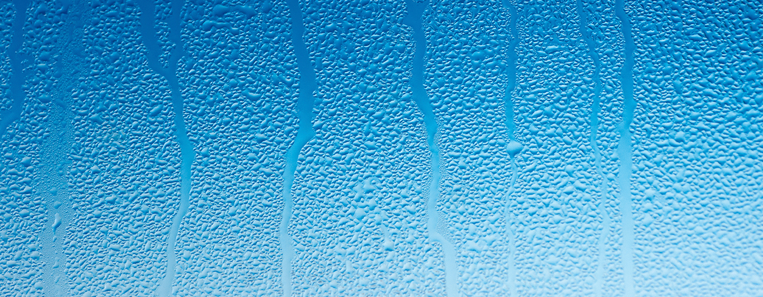 Fukt och kondens på insidan av en ruta med blå himmel i bakgrunden