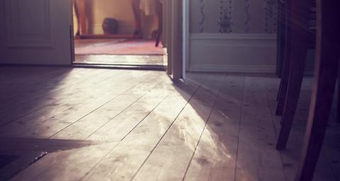 Trägolv i äldre hus med sol i motljus från fönster i angränsande rum