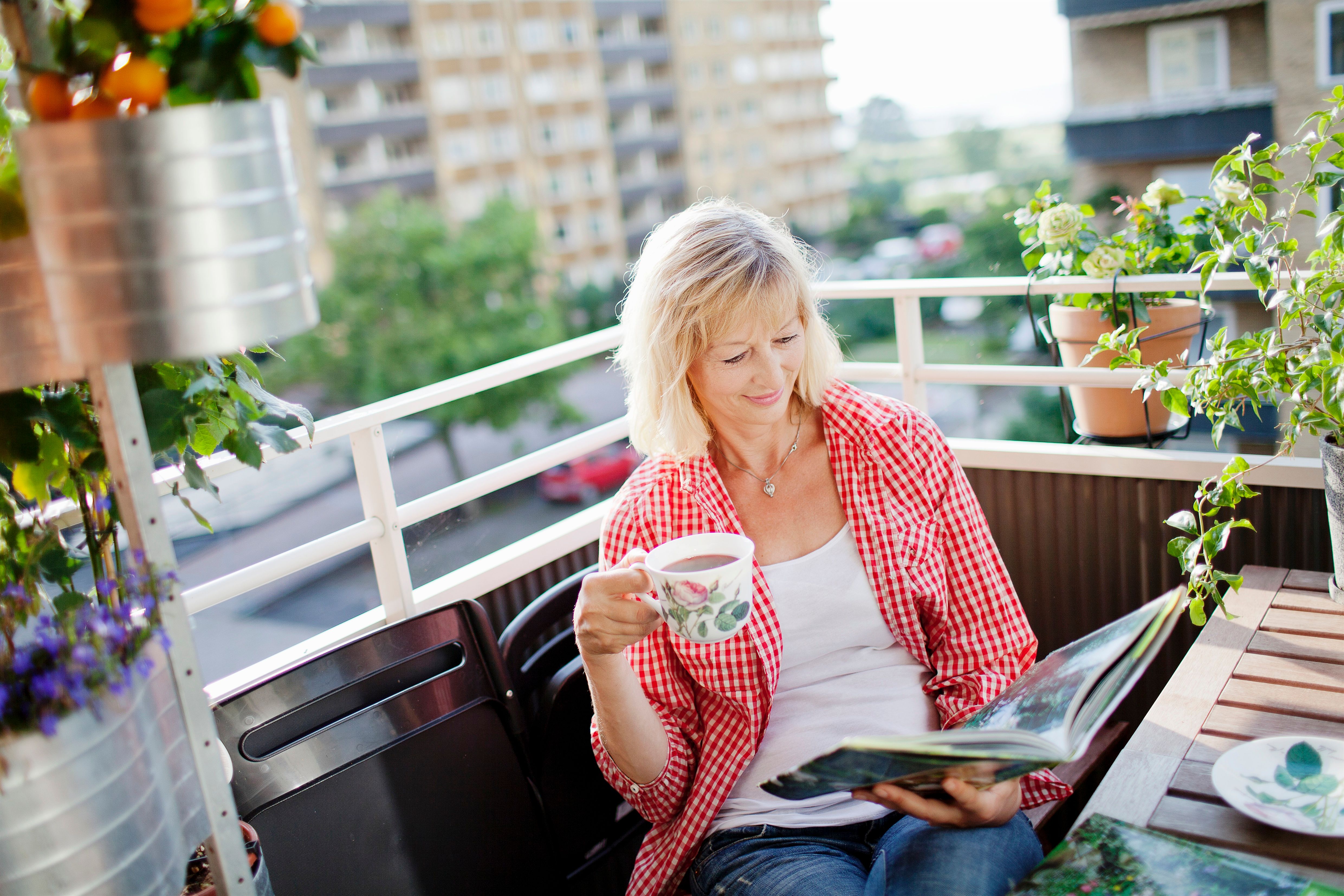 Kvinna på balkong dricker kaffe i sin bostadsrätt