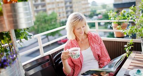 Kvinna på balkong dricker kaffe i sin bostadsrätt efter besiktning