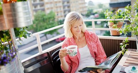 Kvinna på balkong dricker kaffe i sin bostadsrätt efter besiktning