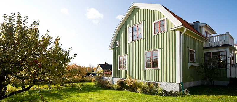 Grönt hus med vita knutar i en grönskande trädgård